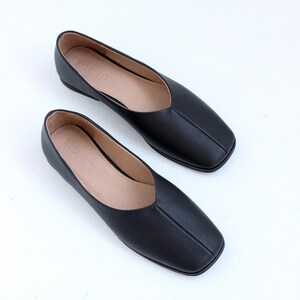 May include: A pair of black leather square-toe flats with a pointed vamp. The shoes have the word "Eternity" written on the insole.
