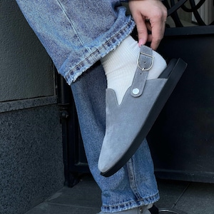 Puede incluir: Zapatos grises de ante con cierre de velcro y suela de goma negra. Los zapatos se llevan con calcetines blancos y pantalones vaqueros azules.