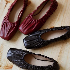 May include: Three pairs of women's flats. One pair is black leather, one pair is burgundy leather, and one pair is black leather with a square toe.