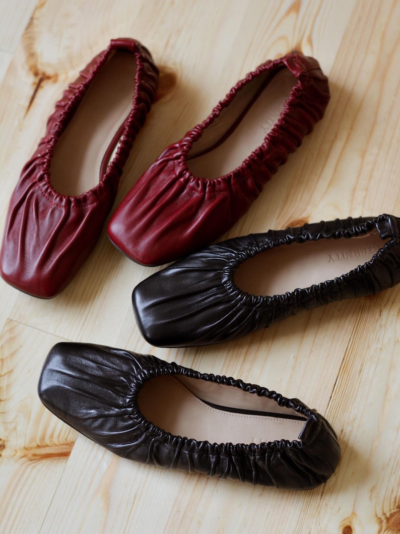 May include: Three pairs of women's flats. One pair is black leather, one pair is burgundy leather, and one pair is black leather with a square toe.