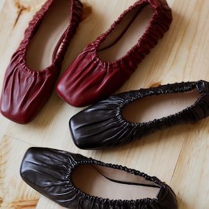 May include: Three pairs of leather ballet flats. One pair is black, and two pairs are burgundy.
