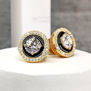 May include: A pair of gold-tone earrings with a black enamel halo and a clear cubic zirconia stone in the center.