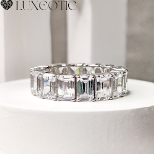 Può includere: Una fascia di eternità in argento con una fila di pietre preziose trasparenti a taglio smeraldo.