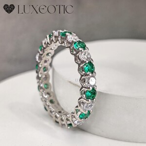 May include: A silver eternity band ring with alternating emerald green and white round gemstones.