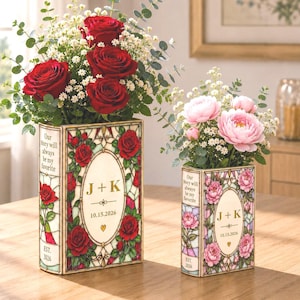 May include: Two rectangular book-shaped vases with stained glass patterns. The larger vase features red roses, while the smaller one has pink peonies. Both are personalized with the text J + K, the date 10.15.2026, and the phrase Our Story will always be my favorite.