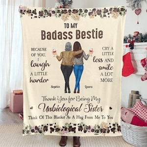 Peut inclure: Une couverture en molleton beige avec un motif floral et le texte "To My Badass Bestie" et "Thank You for Being My Unbiological Sister". La couverture représente deux femmes avec des verres de vin et le texte "Because of you, I laugh a little harder" et "Cry a little less and smile a lot more".
