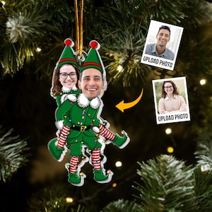 May include: A Christmas ornament featuring two people as elves. The elves are wearing green outfits with red and white striped socks and hats. The ornament has a gold string for hanging and includes the text "UPLOAD PHOTO" on two small photos.