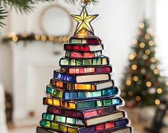 May include: A Christmas tree ornament shaped like a stack of colorful books. The ornament is topped with a gold star and hangs from a gold string. The books have a variety of colors, including red, blue, green, and yellow.