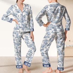 May include: White and blue toile-patterned pyjama set with a dog and landscape design. The long-sleeved top and trousers have blue trim and "DOG MOM" printed on the cuffs. The pyjamas are made of a soft, silky material, perfect for a comfortable night's sleep.