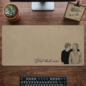May include: Tan rectangular desk mat with a black and white illustration of two people embracing. The words "Best dad ever" are written in cursive. A succulent plant in a terracotta pot and a keyboard are also visible.