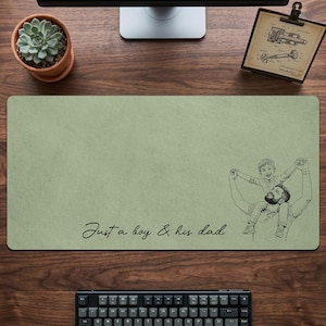 May include: Sage green rectangular desk mat with a black and white illustration of a father and son. The text "Just a boy & his dad" is written in cursive. A keyboard, succulent, and monitor are visible.