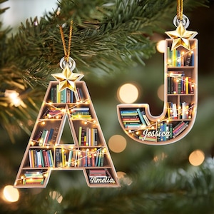 May include: Two wooden Christmas ornaments shaped like the letters A and J. The ornaments are decorated with books and lights. The letter A is labeled "Amelia" and the letter J is labeled "Jessica".