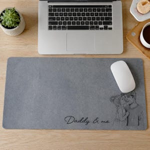 May include: A gray rectangular mousepad with a black and white illustration of a father and child kissing. The words "Daddy & me" are written in cursive. A white computer mouse sits on the pad, next to a laptop.