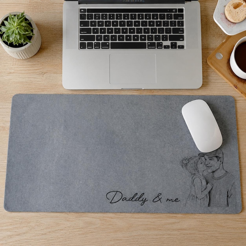 May include: A gray rectangular mousepad with a black and white illustration of a father and child kissing. The words "Daddy & me" are written in cursive. A white computer mouse sits on the pad, next to a laptop.