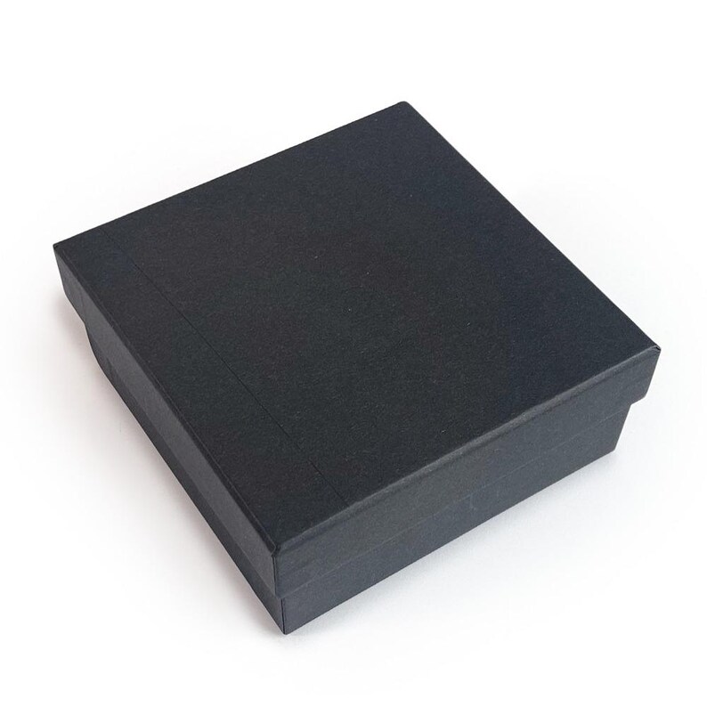 May include: A black, rectangular gift box with a textured surface. The box is closed and has a lid that fits snugly over the base. The box is set against a white background.