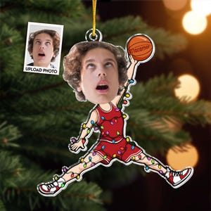 May include: A personalized Christmas ornament featuring a person's face superimposed on a basketball player in a red uniform. The ornament is decorated with colorful Christmas lights and a basketball with the word "Macorner".