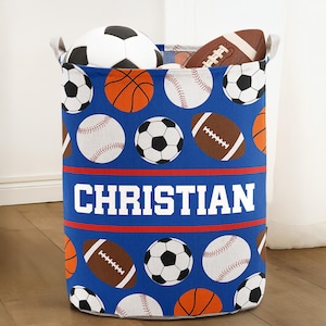 May include: A blue storage bin with a sports theme, featuring soccer balls, basketballs, baseballs, and footballs. The name "CHRISTIAN" is printed in white block letters across the front. The bin is filled with sports balls.