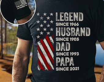 May include: Black t-shirt featuring an American flag design with the words "LEGEND SINCE 1966, HUSBAND SINCE 1985, DAD SINCE 1993, PAPA SINCE 2021." The left sleeve has a small American flag and the text "THE WILLIAM FAMILY."