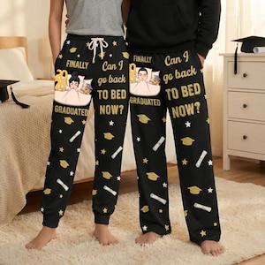May include: Black pajama pants with a graduation theme. The pants feature a repeating pattern of gold graduation caps, stars, and diploma scrolls. Text on the pants reads "FINALLY GRADUATED" and "Can I go back to bed NOW?" with a cartoon image of a person in bed.