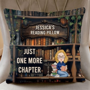May include: A decorative pillow featuring a bookshelf design with the text "Jessica's Reading Pillow" and "Just One More Chapter." The design includes a cartoon illustration of a person reading a book. The pillow is on a neutral-colored chair.