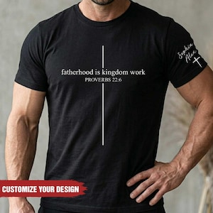 May include: Black t-shirt with the text "fatherhood is kingdom work" and "PROVERBS 22:6" in white. A white vertical line intersects the text. The sleeve has the text "Sophia Alex" and a cross. The bottom of the shirt says "CUSTOMIZE YOUR DESIGN".