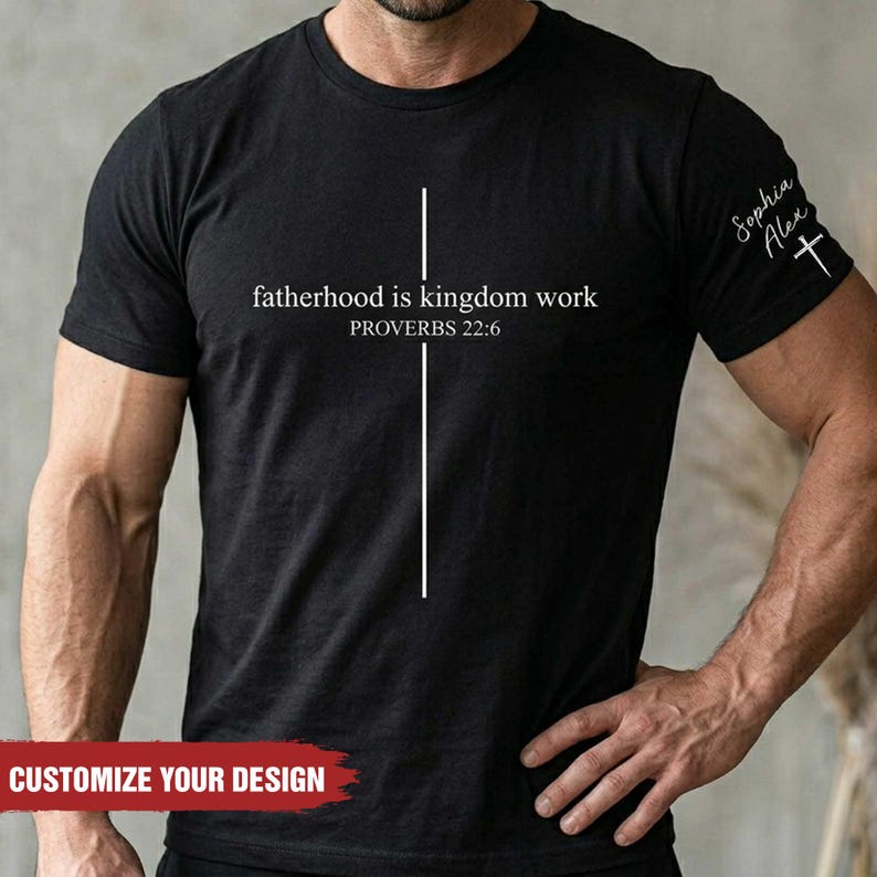 May include: Black t-shirt with the text "fatherhood is kingdom work" and "PROVERBS 22:6" in white. A white vertical line intersects the text. The sleeve has the text "Sophia Alex" and a cross. The bottom of the shirt says "CUSTOMIZE YOUR DESIGN".