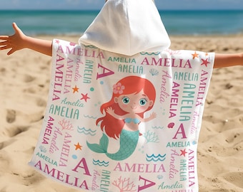 May include: A white hooded beach towel featuring a mermaid illustration with red hair and a teal tail. The towel is personalized with the name "Amelia" in pink and teal, along with starfish and seashell graphics.