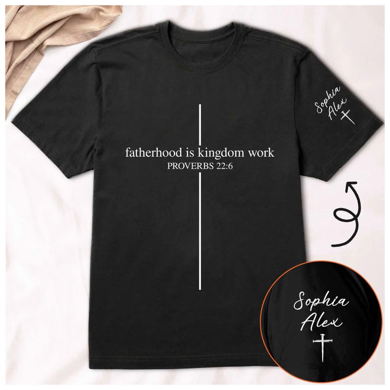 May include: Black t-shirt with the text "fatherhood is kingdom work PROVERBS 22:6" in white. A white vertical line and cross design is centered on the shirt. The sleeve has the name "Sophia Alex" and a cross.
