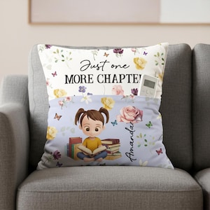 May include: A cushion with a pocket, featuring a cartoon girl reading books. The pillow has a floral design with butterflies and the text "Just one MORE CHAPTER!". A remote control is in the pocket.