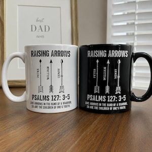 May include: Two ceramic mugs, one white and one black, each with the text "RAISING ARROWS" and the names "PETER", "WILLIAM", and "HENRY" below arrow illustrations. The text "PSALMS 127: 3-5" and a quote are also printed on the mugs.