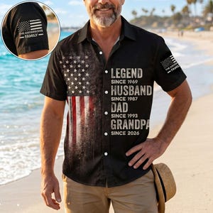 May include: A black short-sleeved button-down shirt featuring a distressed American flag graphic on the left side and white text on the right side reading LEGEND SINCE 1969, HUSBAND SINCE 1987, DAD SINCE 1993, GRANDPA SINCE 2026, with a flag patch on the sleeve.