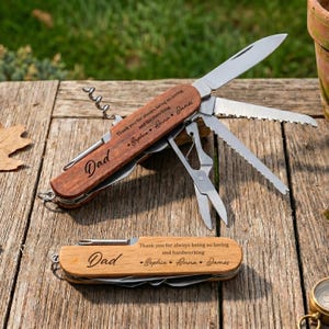 May include: Two wooden multi-tools with various stainless steel tools. One is open, displaying a blade, saw, and scissors. The text "Dad" and a message are engraved on the wood. The closed tool also has the same engraving.