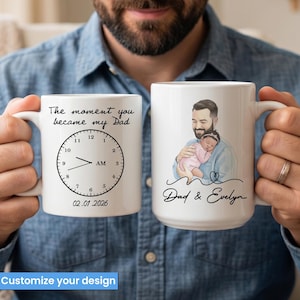 Pode incluir: Duas canecas de cer&acirc;mica branca. Uma caneca apresenta um design de rel&oacute;gio com o texto "The moment you became my Dad" e a data "02.01.2026". A outra caneca tem um desenho de um pai segurando um beb&ecirc;, com o texto "Dad & Evelyn".