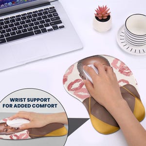 May include: A pink and white wrist rest mouse pad with a woman's face and pink lips printed on it. The text "WRIST SUPPORT FOR ADDED COMFORT" is printed on the bottom left corner of the image.