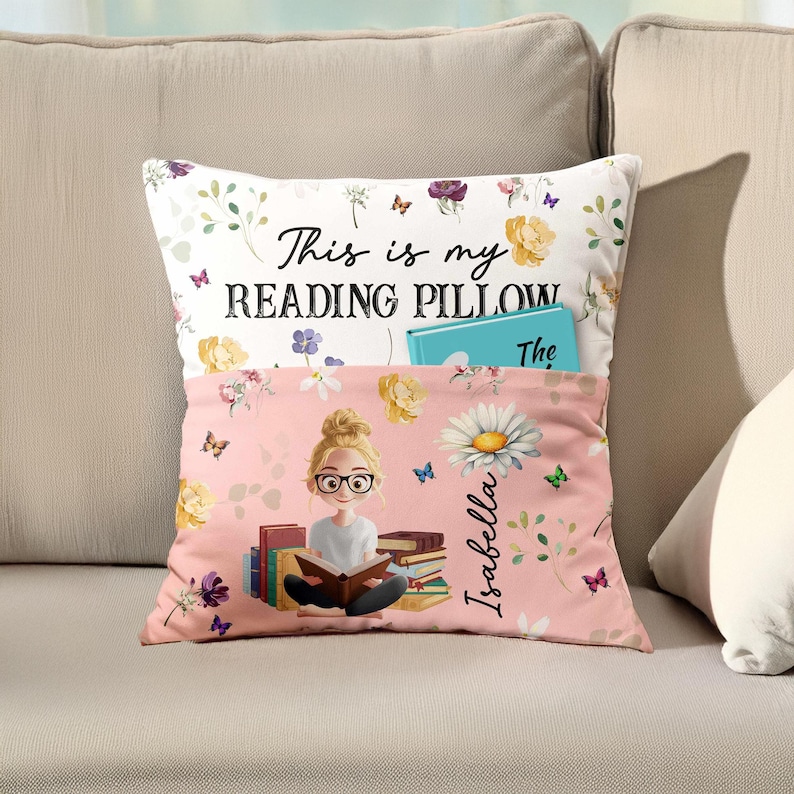 May include: A reading pillow with a pocket, featuring the text "This is my READING PILLOW" and the name "Isabella". The pillow has a floral design with butterflies and a cartoon illustration of a girl reading.