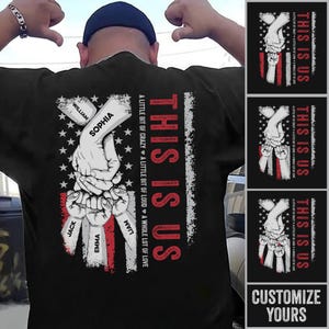May include: Black t-shirt with a graphic design featuring hands holding each other, with the text "THIS IS US" in red and white. The design includes names and the phrase "A little bit of crazy, a little bit of loud, a whole lot of love."
