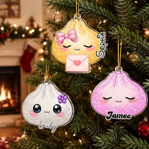 May include: Three acrylic dumpling-shaped Christmas ornaments hanging on a tree. One yellow dumpling with a pink bow and envelope is labeled Sophia. One white dumpling with a purple flower is labeled Emily. One pink dumpling is labeled James.