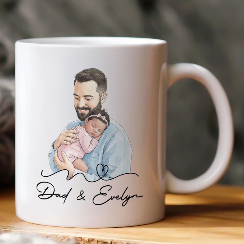 Pode incluir: Caneca de cer&acirc;mica branca com uma ilustra&ccedil;&atilde;o em aquarela de um pai segurando um beb&ecirc; dormindo. A caneca tem o texto "Dad & Evelyn" em uma fonte manuscrita, com um design de cora&ccedil;&atilde;o. A al&ccedil;a &eacute; branca.