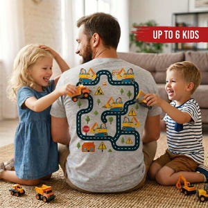 May include: A gray t-shirt with a road and construction vehicle design on the back. The design includes a road, construction vehicles, trees, and road signs. The text "UP TO 6 KIDS" is displayed in a red banner.