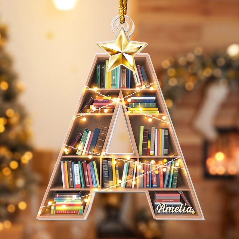 May include: A Christmas ornament shaped like the letter A, with a star on top. The letter is made of wood and has shelves filled with books. The ornament is decorated with white lights and the name "Amelia" is written on the bottom.