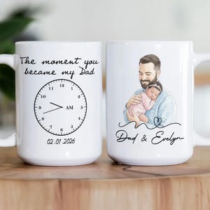 Pode incluir: Caneca de cer&acirc;mica branca com um design personalizado. Um lado apresenta o texto "The moment you became my Dad" com um gr&aacute;fico de rel&oacute;gio e a data 02.01.2026. O outro lado mostra um pai segurando um beb&ecirc;, com o texto "Dad & Evelyn".