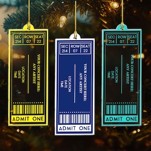 May include: Three concert ticket ornaments in yellow, blue, and teal, hanging from gold strings. Each ticket has the text "SEC ROW SEAT 214 07 22", "YOUR CONCERT HERE: ANY ARTIST", and "ADMIT ONE".