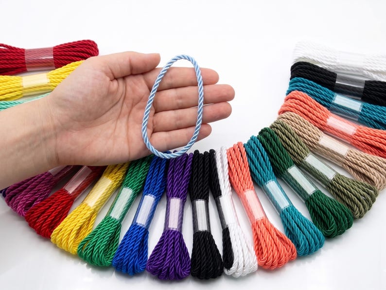 May include: A variety of colorful twisted cords, including red, yellow, green, blue, purple, black, white, and coral. A light blue cord is held in a hand. The cords are bundled and wrapped with clear plastic.