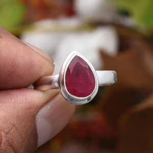 以下が含まれることがあります： 洋梨型のファセットルビーをあしらったスターリングシルバーリング。鮮やかな赤色のルビーはベゼルセッティングで、その色と輝きを際立たせています。リングのバンドは滑らかで磨かれており、クラシックでエレガントなデザインです。