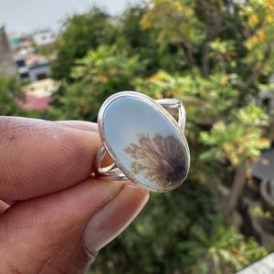 Puede incluir: Anillo de plata con una piedra ovalada que presenta un patrón dendrítico en tonos marrones y grises. La banda del anillo tiene un diseño dividido, lo que agrega un toque único a la joya.