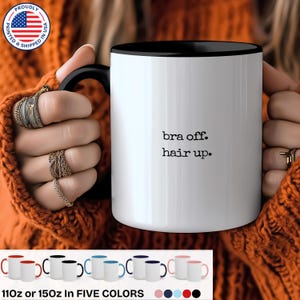May include: White ceramic mug with a black rim and handle. The mug has the text "bra off. hair up." printed in black.