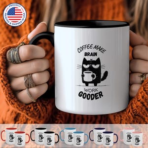 May include: White ceramic coffee mug with a black rim and handle. The mug features a black and white illustration of a cat holding a cup of coffee. The text "Coffee Make Brain Work Gooder" is printed on the mug.
