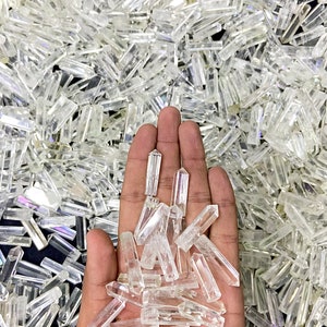 May include: A hand holding a pile of clear quartz crystal points. The points are of various sizes and shapes, and they are all very clear and shiny.