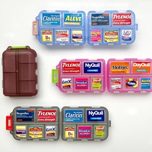 May include: Three multi-compartment plastic pill organizers in blue, pink, and gray, plus one closed dark brown case. Each organizer contains various labeled medication packets including Tylenol, Claritin, Aleve, NyQuil, Motrin, DayQuil, and others.