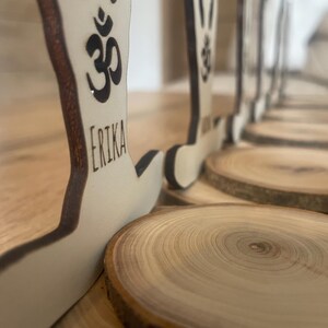 K&ouml;nnte beinhalten: Ein Satz Holzfiguren in Yoga-Posen mit dem Om-Symbol und Namen auf jeder Figur. Die Figuren stehen auf Holzscheiben.